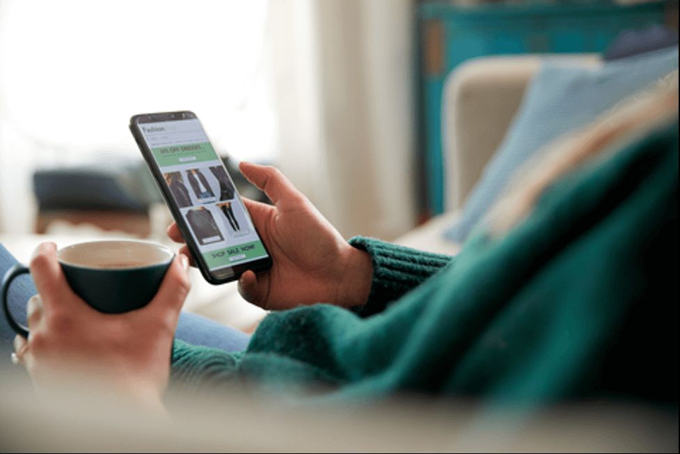 Hands holding a smartphone showing a shopping app, next to a cup of coffee
